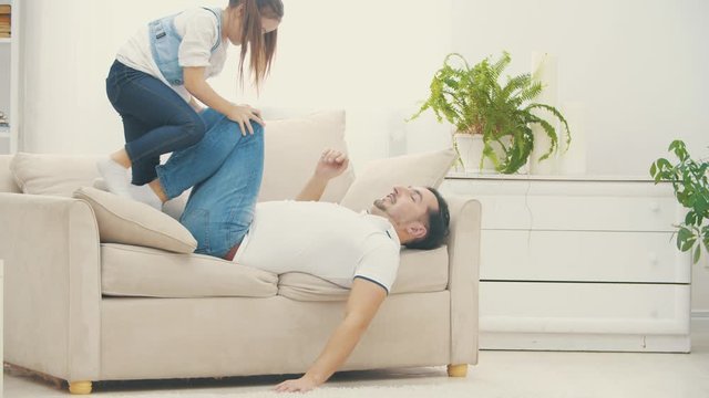Father is tiered after playng with her little daughter on white sofa in 4K slowmotion video.