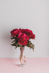 Obraz premium Vertical shot of fresh red peony flowers in a vase on a beautiful surface