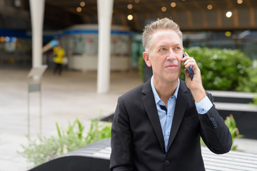 Mature businessman talking on the phone while sitting in the city outdoors