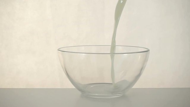 Milk is poured and splashed in slow motion into a transparent bowl on a white background.