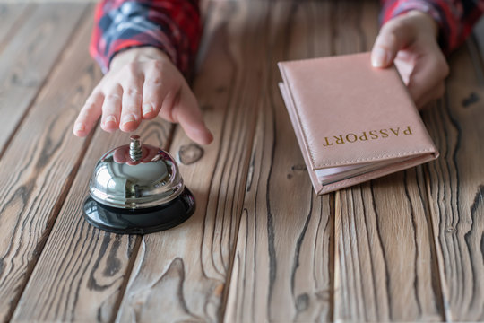 Woman using passport for registration in the hotel. Silver vintage bell on wooden rustic reception desk. Hotel service.