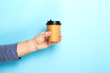 Male holds hand paper cup with coffee on blue background