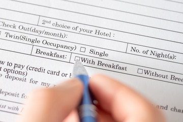 Woman filling hotel reservation form check mark choosing breakfast in hotel service. Reception desk, registration. Close up. Selective focus.