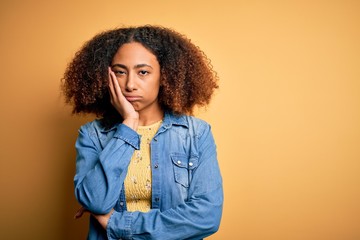Young african american woman with afro hair wearing casual denim shirt over yellow background thinking looking tired and bored with depression problems with crossed arms.