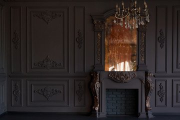 Decorative fireplace, vintage mirror and chandelier in classical black room interior