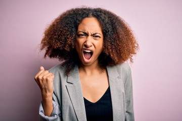 Young african american businesswoman with afro hair wearing elegant jacket angry and mad raising fist frustrated and furious while shouting with anger. Rage and aggressive concept.
