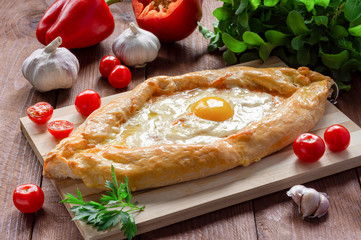 Khachapuri in Adjarian. Traditional Georgian cuisine. Open pie with Suluguni cheese and egg yolk in the shape of a boat on a wooden Board.