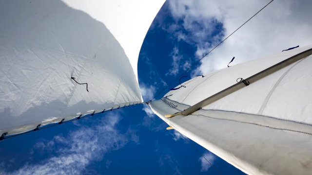 white sail in the wind against a blue sky with clouds in sunny weather
