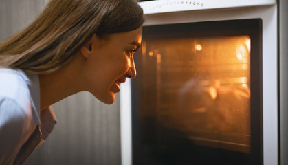 Fototapeta na wymiar Young housewife watching her lunch in oven at kitchen