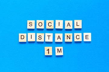 Words social distance 1 m. Wooden inscription on a blue background. Information sign of social distance 1 m from blocks on a blue background.