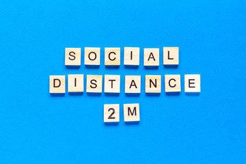 Words social distance 2 m. Wooden inscription on a blue background. Information sign of social distance 2 m from blocks on a blue background.