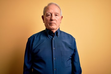 Obraz premium Grey haired senior man wearing casual blue shirt standing over yellow background Relaxed with serious expression on face. Simple and natural looking at the camera.