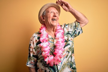 Grey haired senior man wearing summer hat and hawaiian lei over yellow background very happy and...