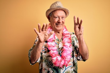 Grey haired senior man wearing summer hat and hawaiian lei over yellow background showing and...