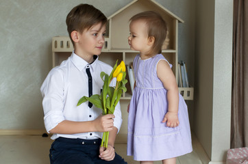 Big brother congratulating his little sister with a bouquet of yellow tulips. Blonde boy with a...