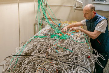 Communication concept. A technician untangles a lot of cables on a false ceiling. A man is laying Internet wires in a server room. Random chaotic plexus of wires.