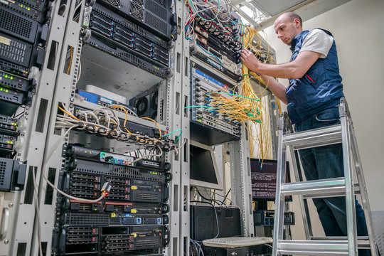 The specialist works in the server room of the data center. Worker lays communication cables. Technological concept. Technician standing on a ladder connects internet wires.