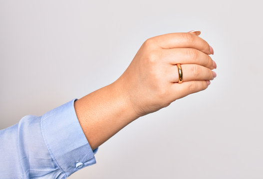 Hand of caucasian young woman holding golden marriage ring over isolated white background