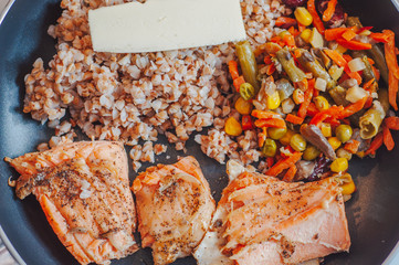 The athlete's lunch is warmed up in a pan. Buckwheat, salmon and vegetables.