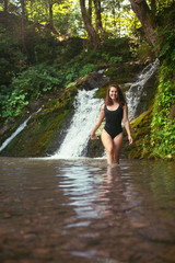 gorgeous woman in sexy black swimsuit in front of waterfall