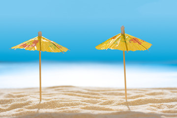 Sun umbrellas on sandy beach with blurry blue ocean and sky. Social distancing or COVID-19 protection at summer holidays. Summer background. Soft focus
