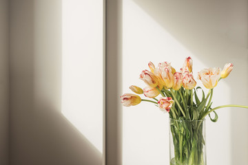 Yellow tulip flowers bouquet in glass vase against the white wall. Holiday celebration concept. Interior decoration.