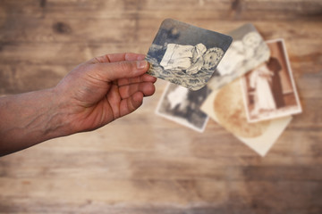 old man’s male hands hold old retro family photos over an album with vintage monochrome...