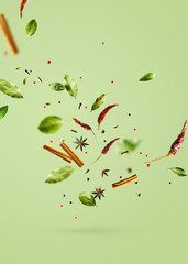 Flying spices bay leaf, red chili pepper, anise, cinnamon sticks on a green background.