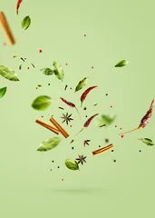 Zelfklevend Fotobehang Flying spices bay leaf, red chili pepper, anise, cinnamon sticks on a green background. © PINKASEVICH