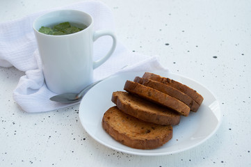 A white mug herbal tea with fresh currant leaves and sweet breadcrumbs on a white plate on a white background.