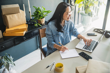 Young business woman working online e-commerce shopping at her shop. Young woman seller prepare...