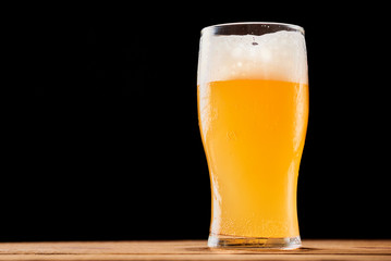 Glass of wheat beer with foam on the dark background