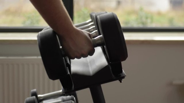 Strong male hand puts on a support a big dumbbell.