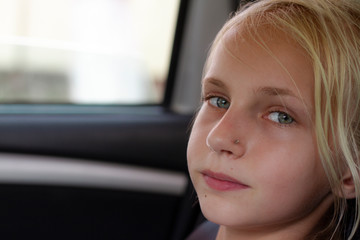Fototapeta na wymiar Closeup portrait of a relaxed and calm car passenger. A beautiful young blond girl is enjoying the journey in the car. Copy space. Travel by car. Portrait of cute child at the window of a moving auto.