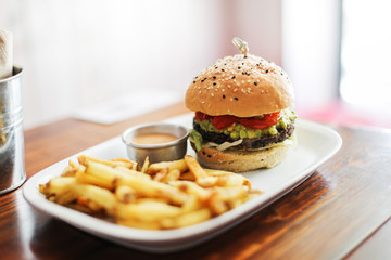 Fresh burger with avocado, sauce, french fries on a wooden table in a cafe next to a window