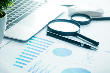 A desk, White table with a computer, a graph, a magnifying glass and a calculator.