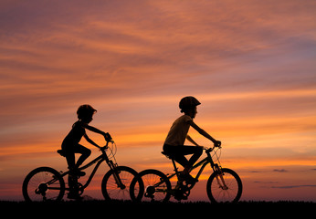 silhouettes of children on bicycles against the background of the sunset