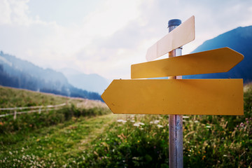 Yellow empty signboard with pointer against beautiful mountains landscape, Tirol Alps, Austria.