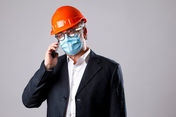ingegnere con caschetto di protezione vestito con giacca e camicia indossa un a mascherina facciale chirurgica, telefona con il suo cellulare, isolato su sfondo bianco 