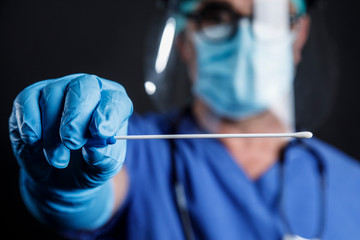 Medico  con protezioni e camice blu mostra un tampone faringeo per controllare lo stato di salute ,...