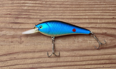 closeup of one blue fishing lure with two fishing hooks isolated on wooden background