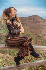 Woman leaning on a wooden beam dressed in a steampunk suit in a defiant attitude with her arms...