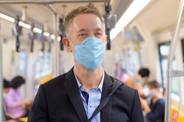 Face of mature businessman with mask standing with distance inside the train