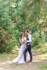 An attractive newlywed couple, a happy and joyful moment. A man and a woman shave and kiss in holiday clothes. Bohemian-style wedding cermonia in the forest in the fresh air.