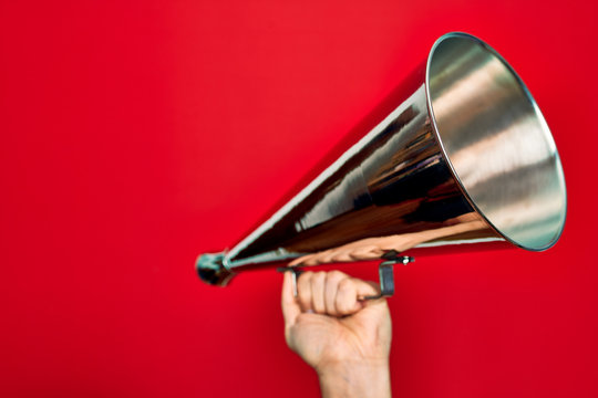 Beautiful hand of man holding vintage megaphone over isolated red background