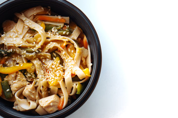 Stir fry noodles with vegetables and chicken in black bowl. Isolated. Top view. Copy space.