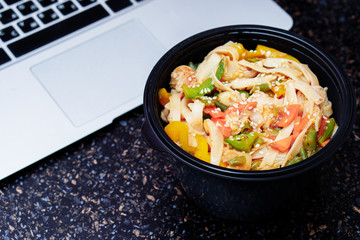 Stir fry noodles with vegetables and chicken in black bowl. Stone background. Top view. Copy space.