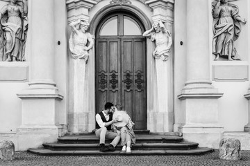 A young woman and a man hug and kiss while sitting on the steps of an old building.