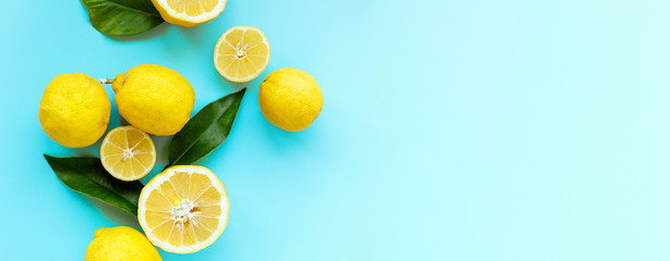 Ripe juicy lemons and green leaves on bright blue background. Lemon fruit, citrus minimal concept,...