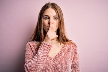 Young beautiful redhead woman wearing casual sweater over isolated pink background asking to be quiet with finger on lips. Silence and secret concept.